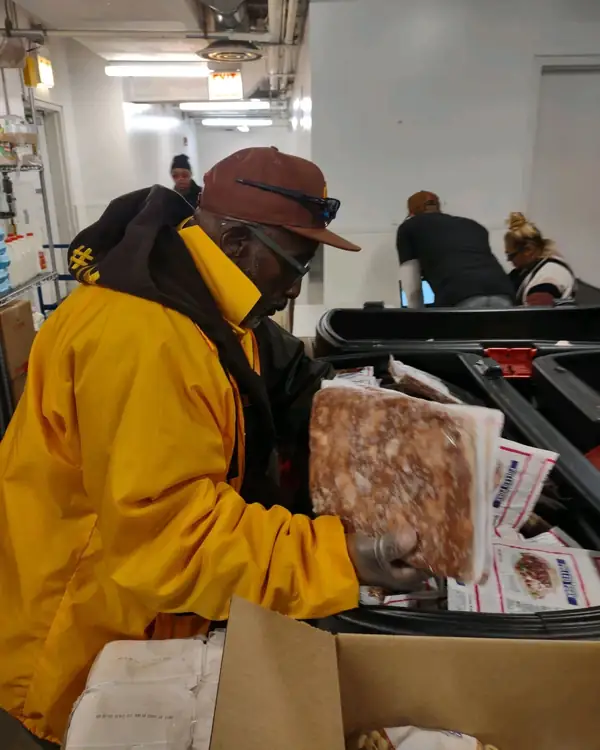 Brother Kenneth William, in a gold Iota Phi Theta jacket, packing food boxes at a Chicago food pantry